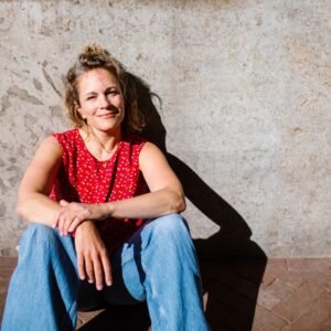 woman with blonde hair sitting along wall with red shirt and jeans