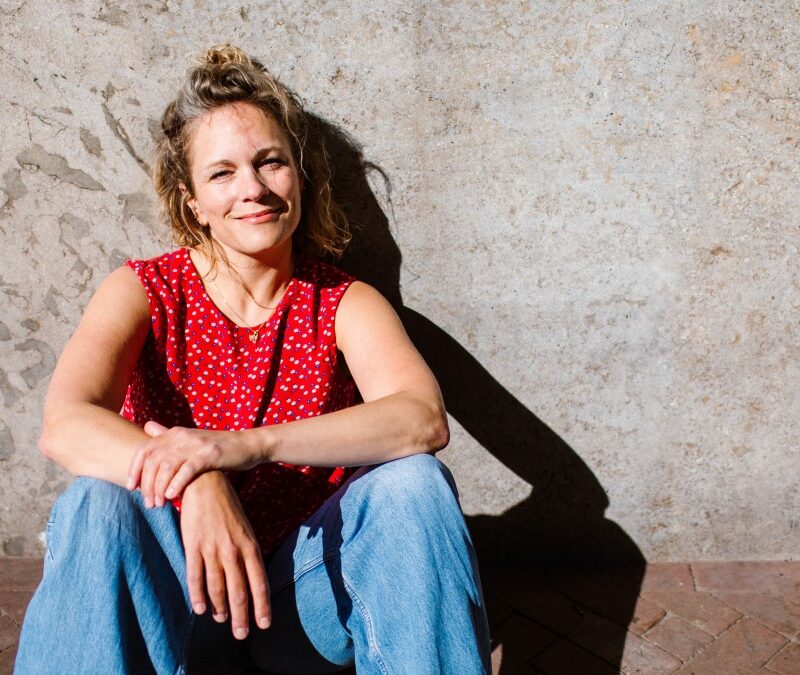 woman with blonde hair sitting along wall with red shirt and jeans